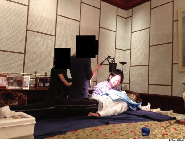 Four people inside Jeffrey Epstein’s dining room: one lying on a table, one seated and two standing, all of their faces obscured except for the seated persons.