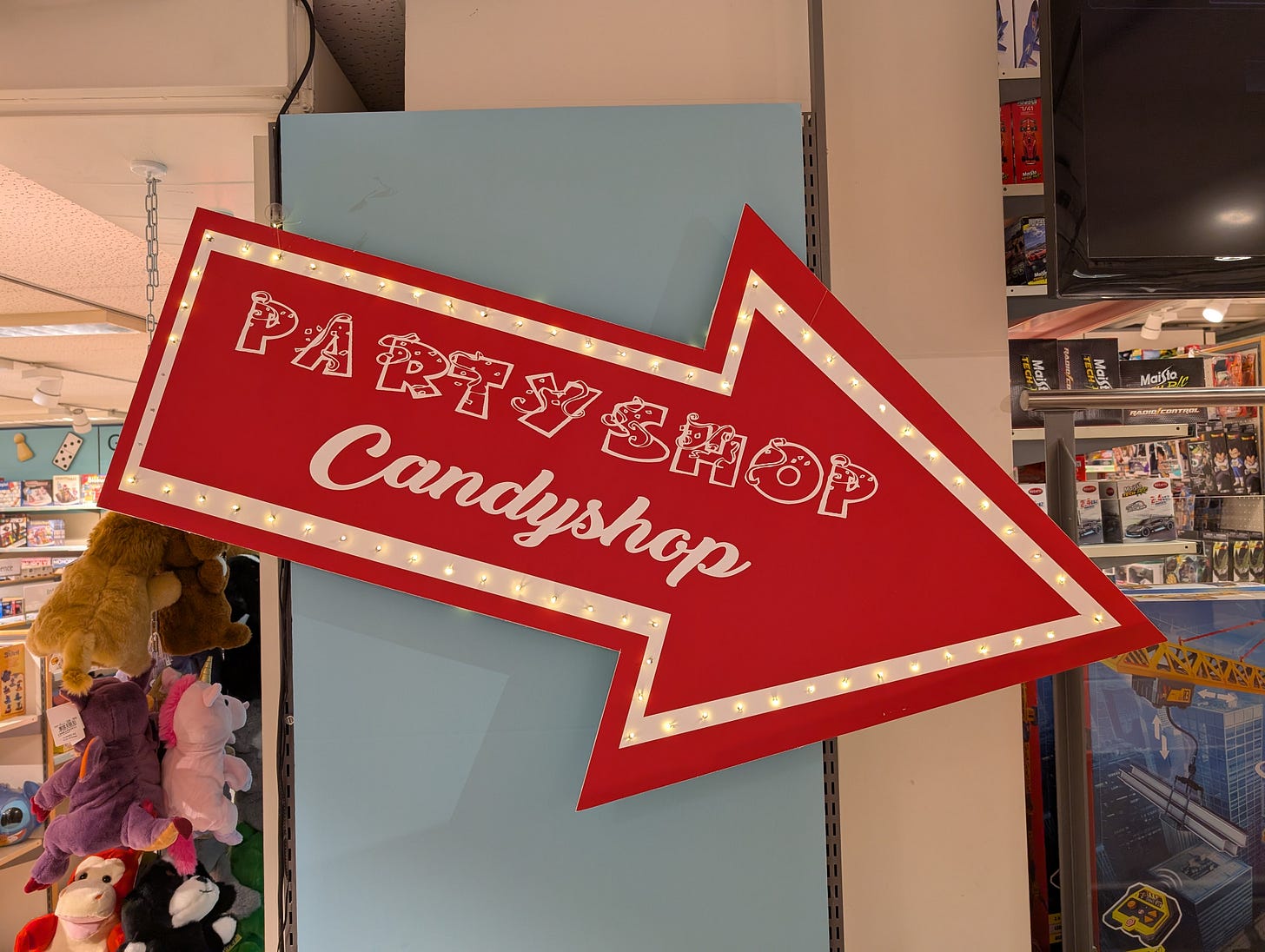 Large red sign in the shape of an arrow readnig "Party Shop Candyshop"