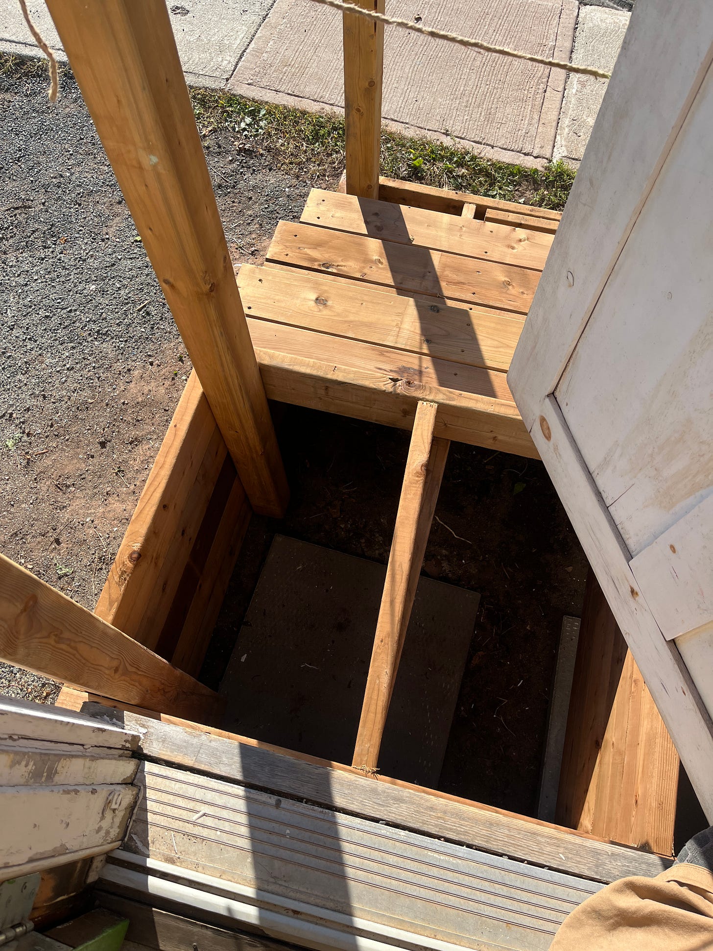 A photo looking out my front door at our new wooden steps, still under construction. The top layer of the platform at the top doesn't have planks across it yet, so you can see down into the dark hole left behind.