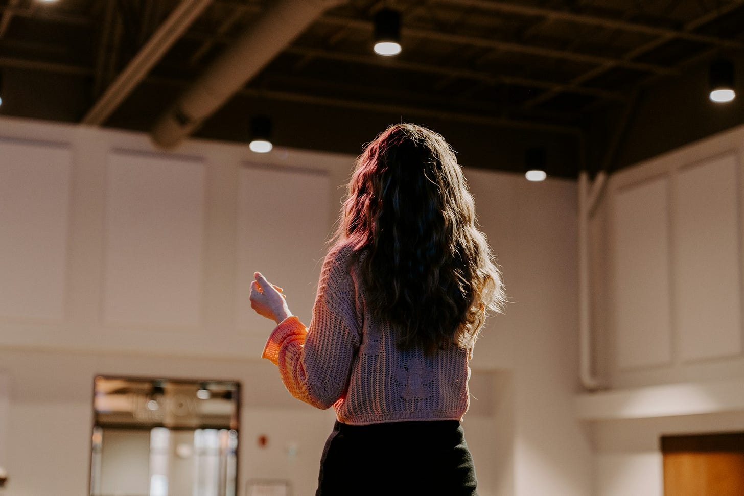 Seen from behind, a woman speaks in a large room. Photo by Kelly Sikkema on Unsplash