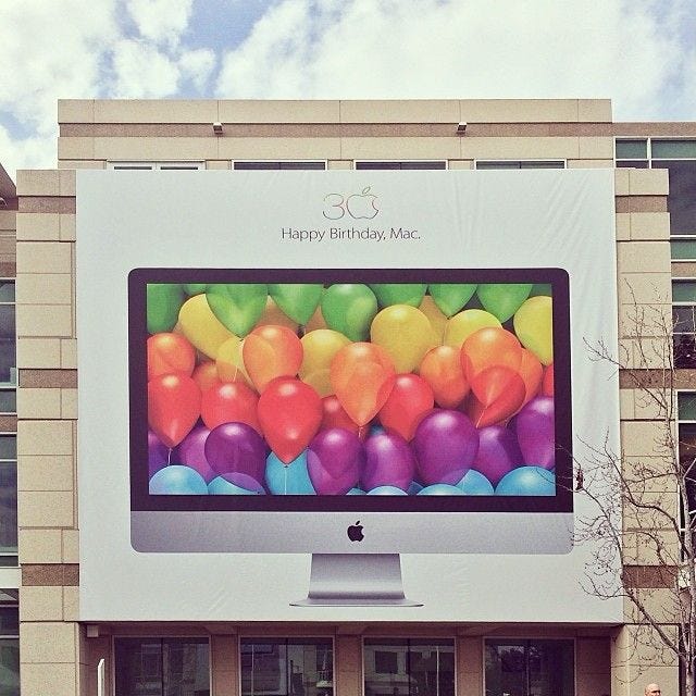 Giant poster of iMac with balloons on the screen and the words "Happy birthday, Mac" above the computer.