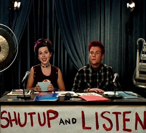 This may contain: two people sitting at a table in front of microphones with the words shut and listen written on it