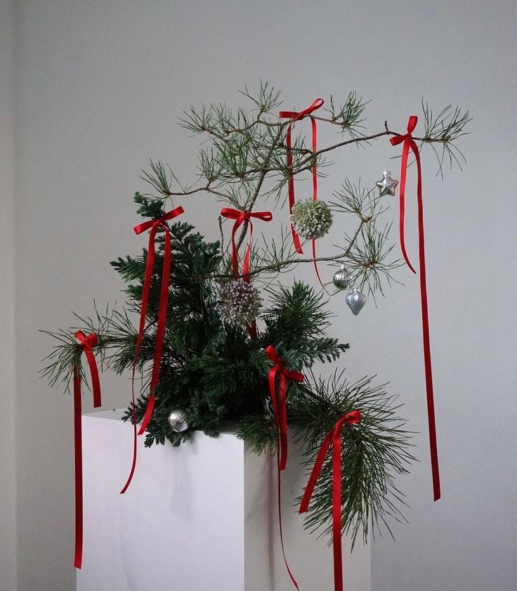 This may contain: a white vase filled with pine branches and red ribbon hanging from it's sides
