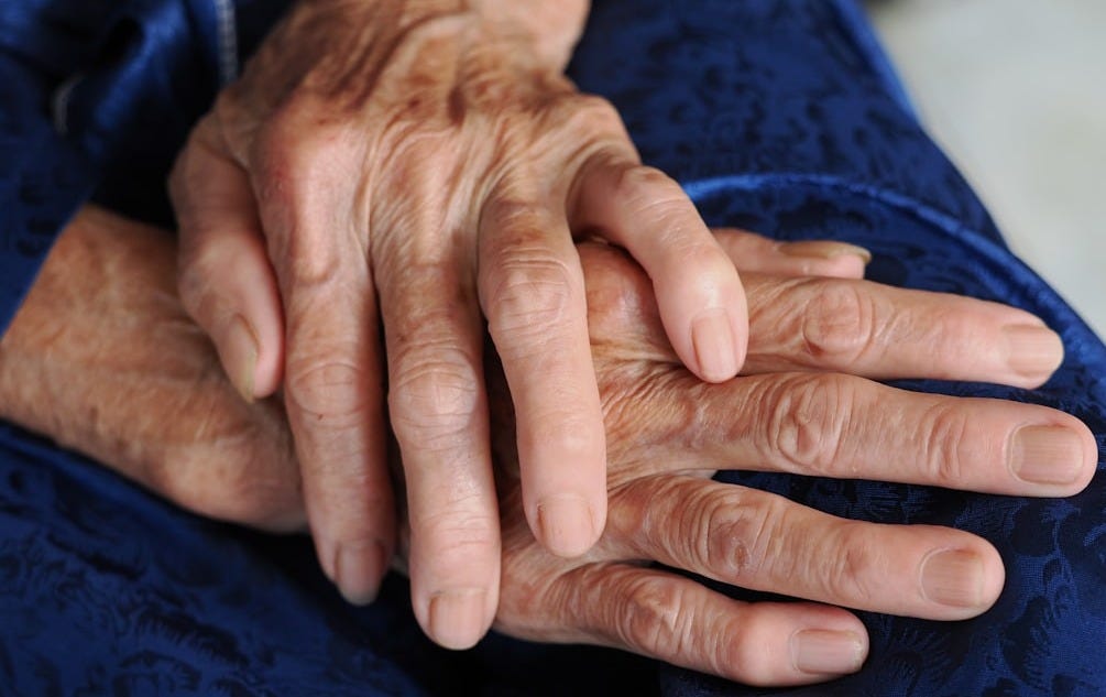 Close-up of elderly hands resting on a blue fabric.
