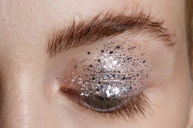 A close up image of an eye with silver glitter on the eyelid and no mascara