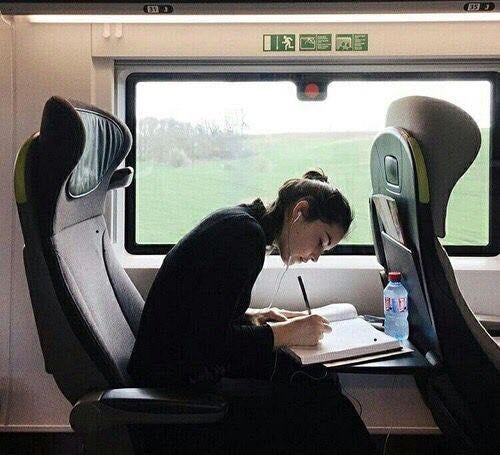 This may contain: a woman writing on a paper while sitting in a seat next to an open window