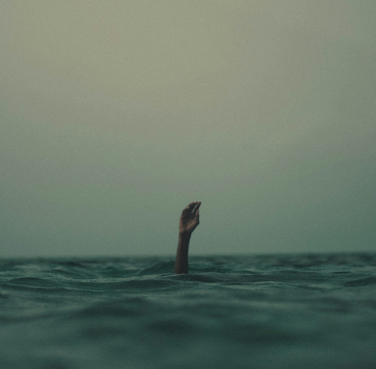 A hand poking through the water surface, of a person seemingly drowning in the ocean.