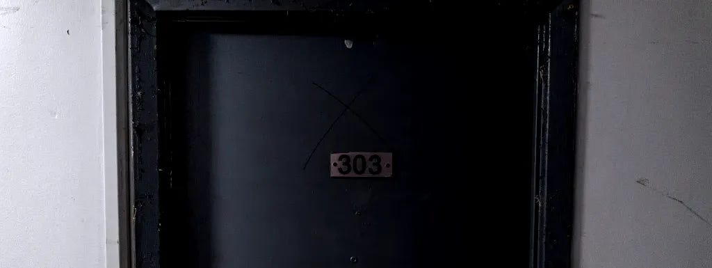 A door with three X’s drawn on it. The doorknob is broken and dangling.