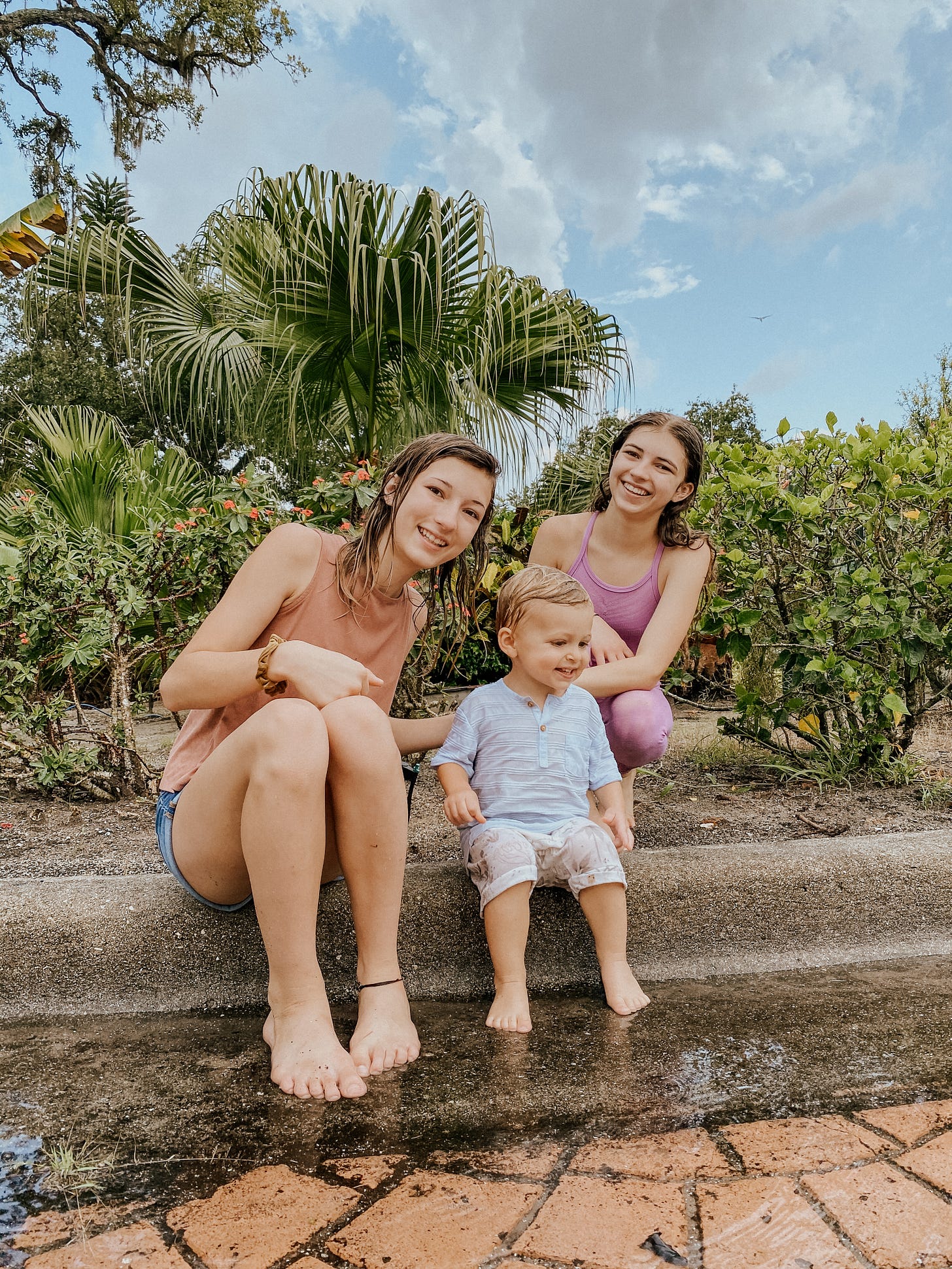 Three smiling kids enjoying a rainy summer day barefoot near puddles—perfect inspiration for cozy, screen-free rainy day activities for kids featured in Foxie and June’s free printable.