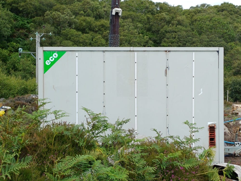 A grey-white metal box with 'eco' in one corner, bracken in front.