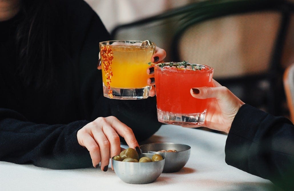 a woman sitting at a table with a bowl of olives and a drink a woman sitting at a table with a bowl of olives and a drink