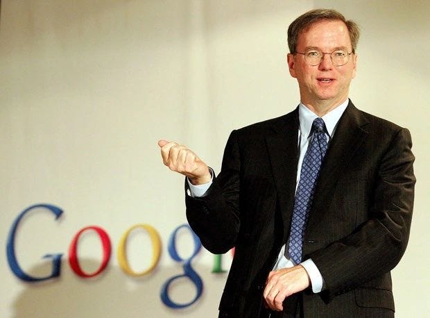 Eric Schmidt in a suit gesturing in front of a blurred Google logo Eric Schmidt in a suit gesturing in front of a blurred Google logo