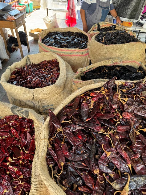 A nine image gallery showing dried chiles, coffee, cocoa beans, and sugar for sale at the market.