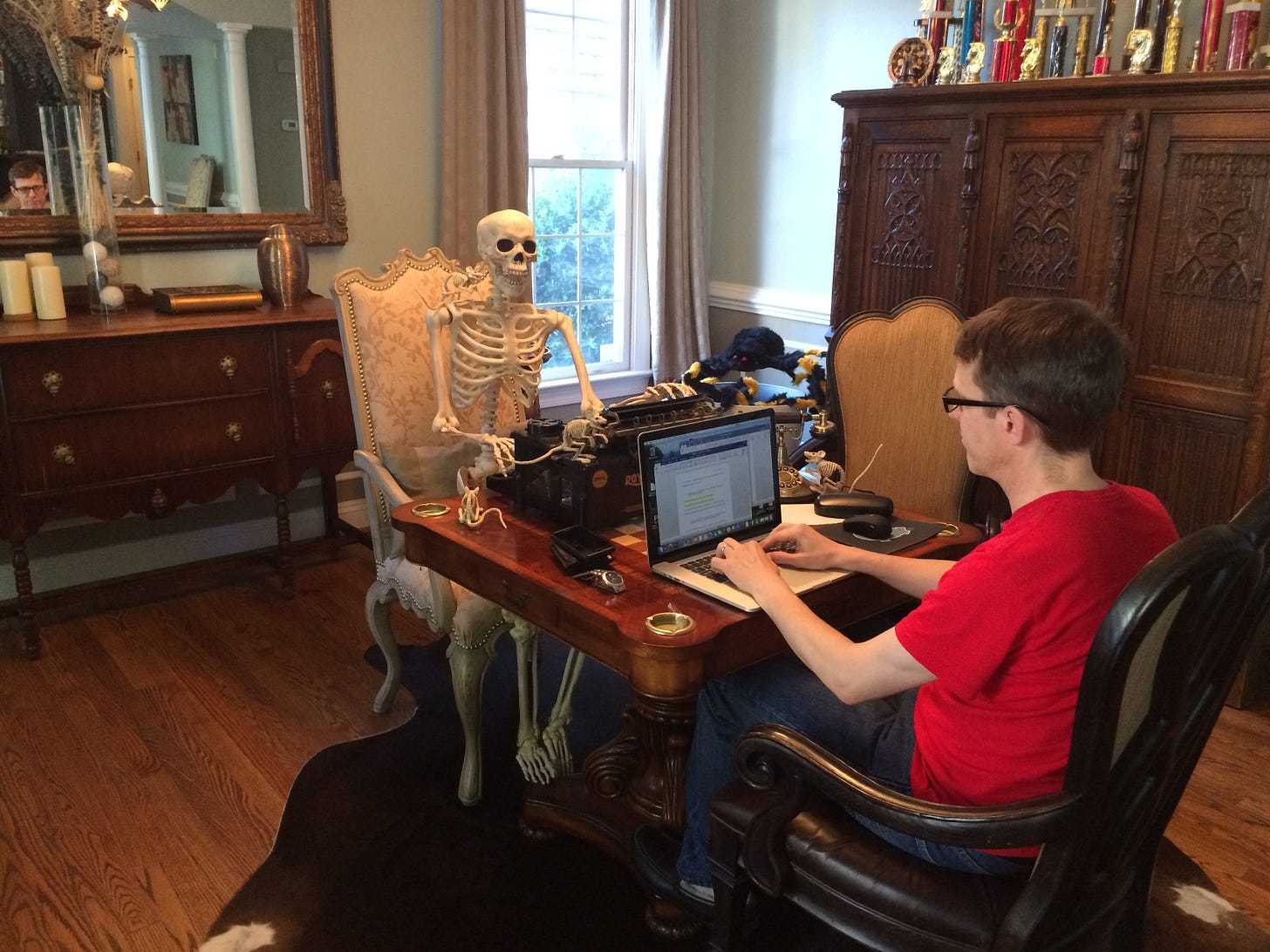 Russell Carr typing a story into his laptop opposite a skeleton typing on an old typewriter