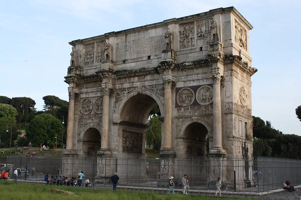 A picture of the arch. A number of tourists walk near the base of the arch and appear small, giving a sense of the triumphal arch's scale.