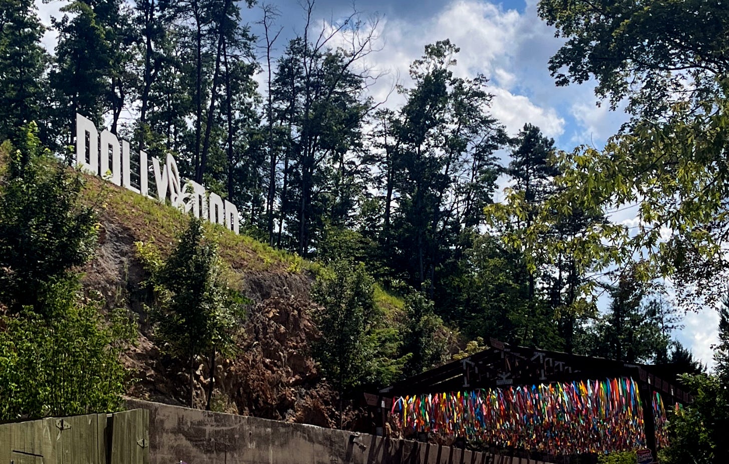 The “Dollywood” sign, modeled after the Hollywood sign, is shown on a hilltop at the Dollywood amusement park in Pigeon Forge, Tennessee. An installation of rainbow banners flies in the foreground.