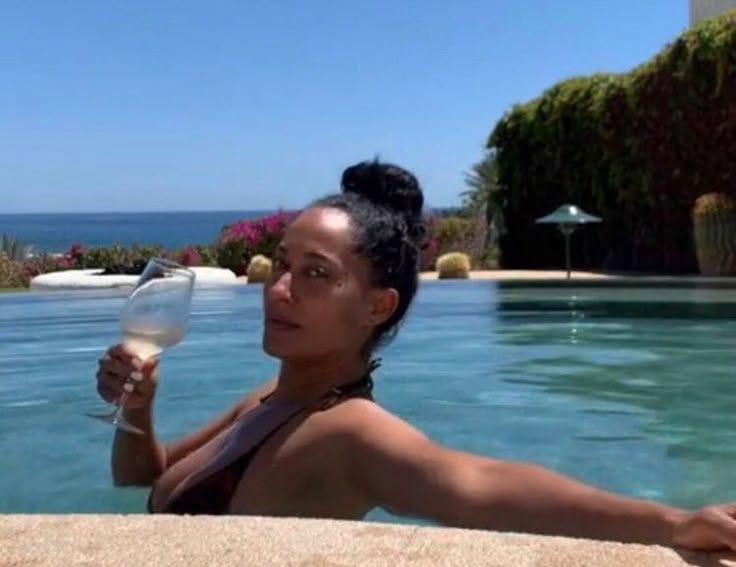 This may contain: a woman holding a wine glass next to a swimming pool with the ocean in the background