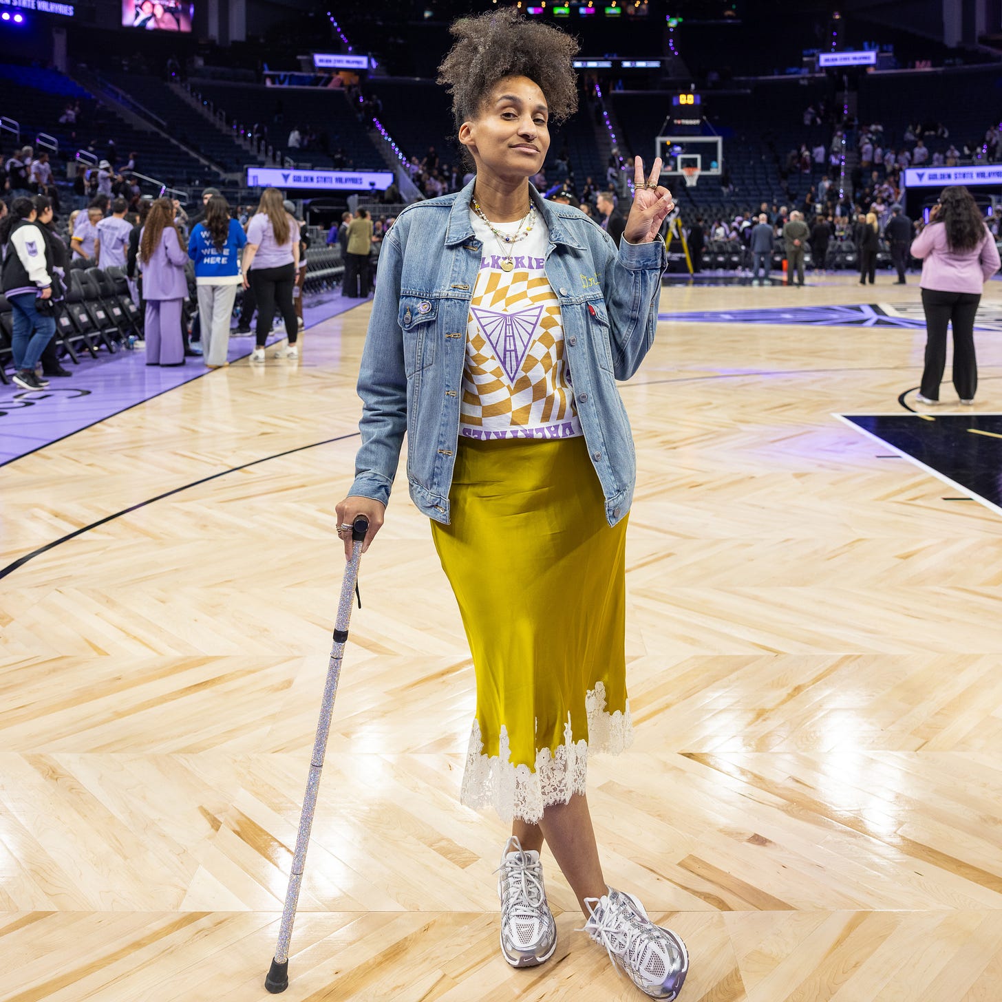 Dr. Cadet poses courtside at a Valkyries game wearing a yellow skirt, jean jacket, metallic purple sneakers and her rhinestone cane. Photo by Chloe Jackman.