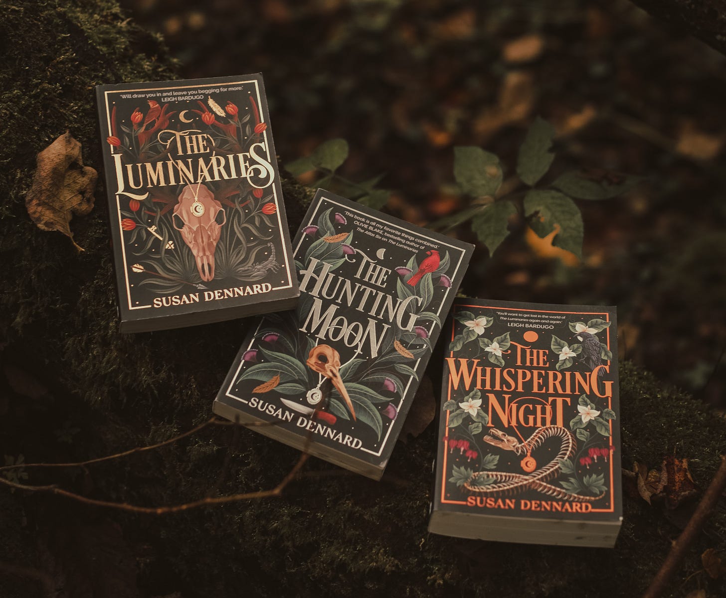 Finished UK copies of the Luminaries series on a mossy log with heavy forest vibes