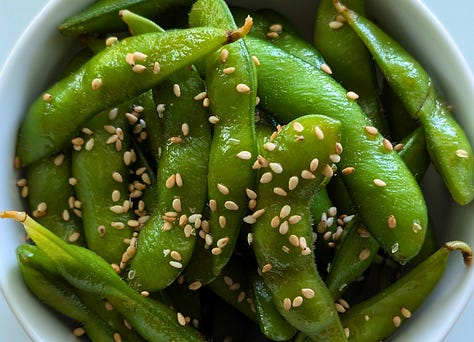 Three close-up images of cooked edamame: one tossed with sesame oil, soy sauce, and sesame seeds; one with shichimi togarashi and lime; and one with melted butter and furikake.