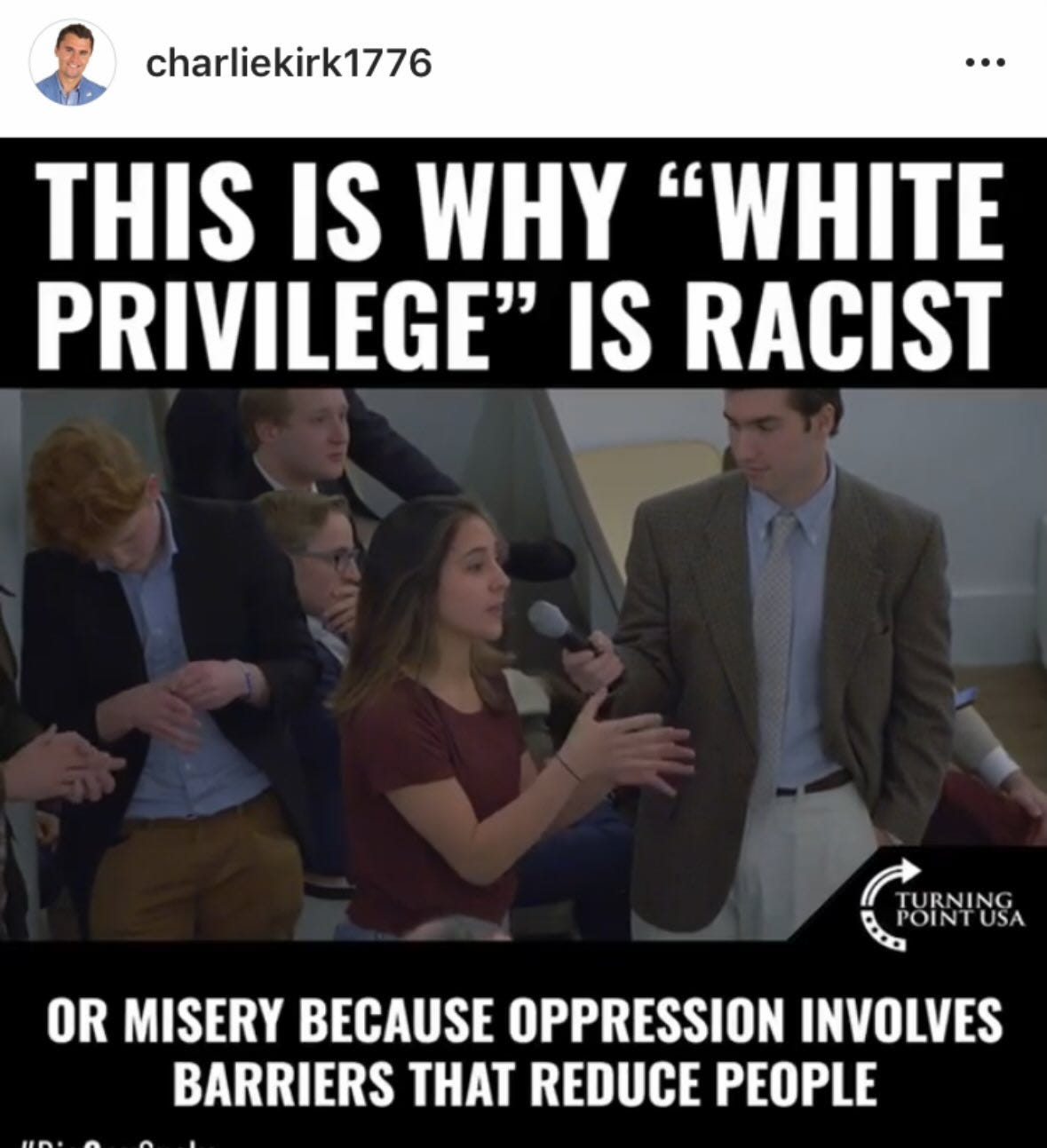 Charlie Kirk standing and speaking, holding a microphone, wearing a suit and tie. A group of young people, including a girl in a red shirt gesturing, are visible in the background. Text overlay reads "THIS IS WHY \"WHITE PRIVILEGE\" IS RACIST OR MISERY BECAUSE OPPRESSION INVOLVES BARRIERS THAT REDUCE PEOPLE" with a Turning Point USA logo.