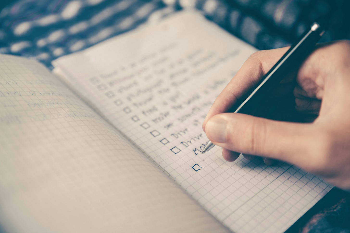 A person writing out a checklist on graph paper. Only the hand and pen is visible in the photo. A person writing out a checklist on graph paper. Only the hand and pen is visible in the photo.