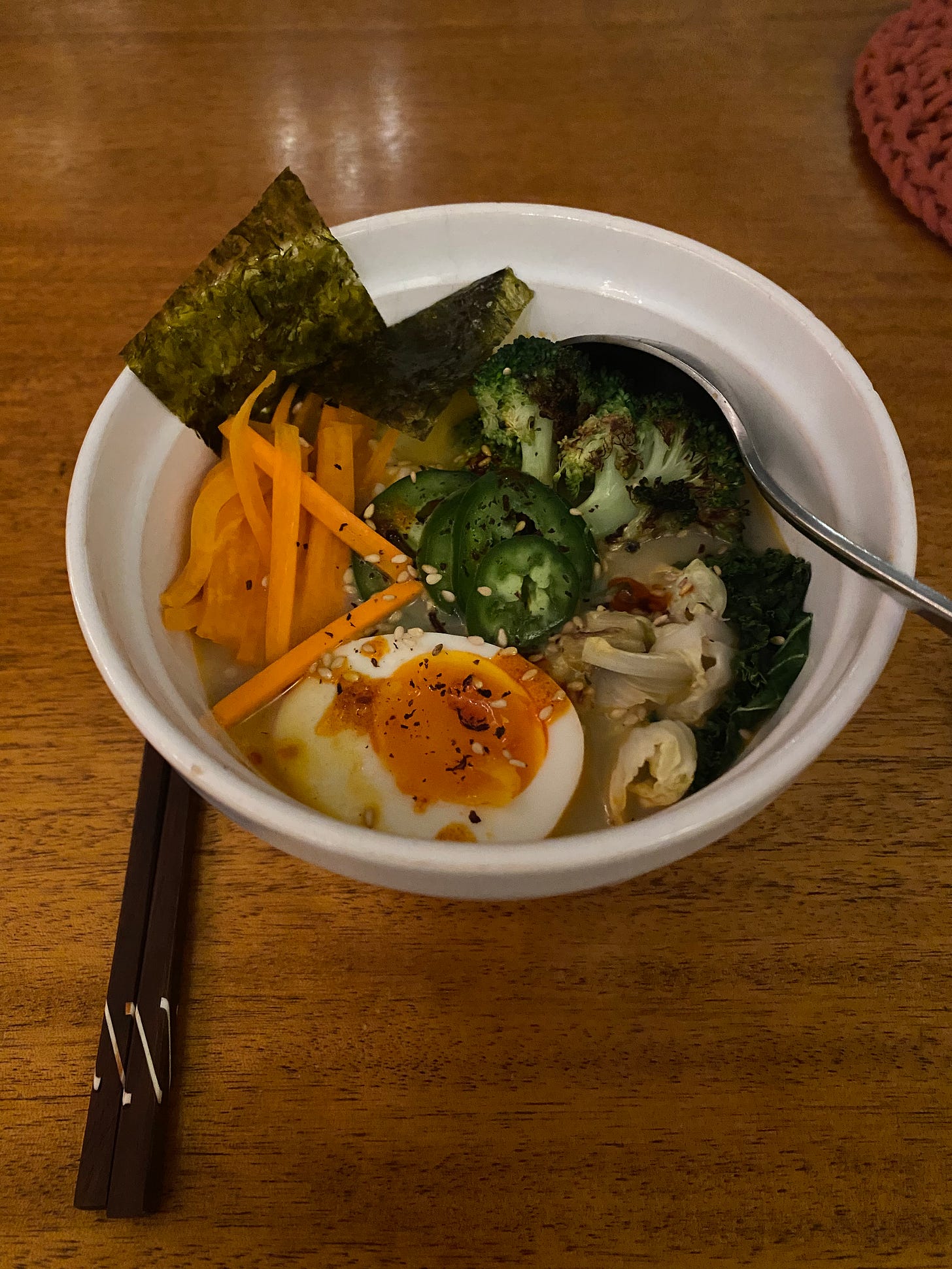 A bowl of ramen in a creamy broth, with wilted cabbage, seared broccoli, carrot matchsticks, jalapeño slices, seaweed, and half a soft-boiled egg. It's sprinkled with furikake and chili oil.