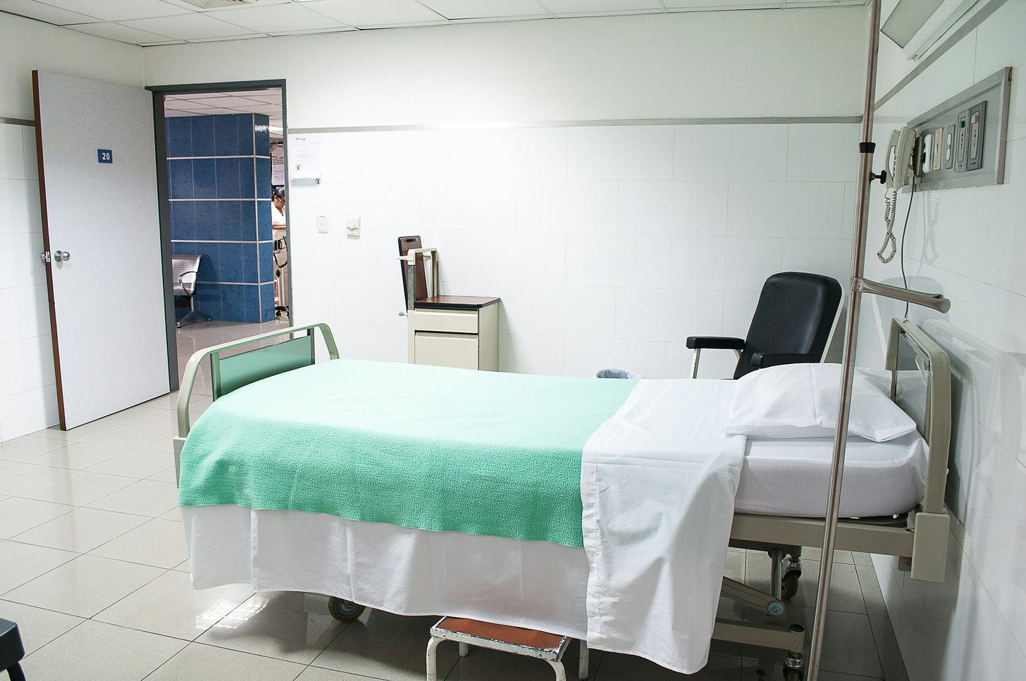 A plain hospital room with a bed covered by a green blanket. A plain hospital room with a bed covered by a green blanket.