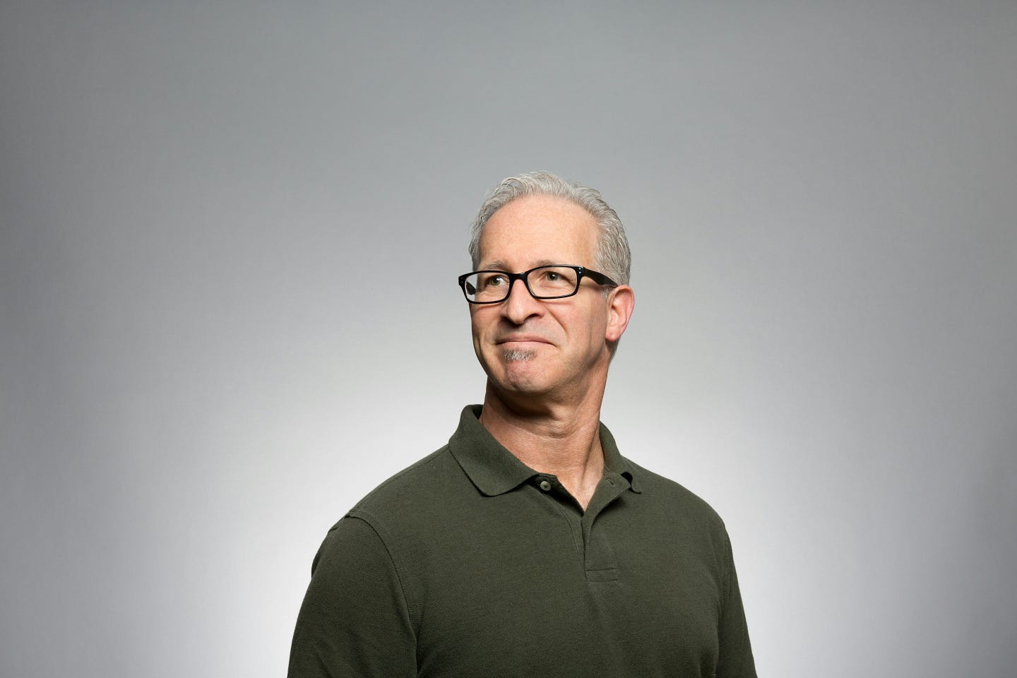 A caucasian male with gray hair and black glasses in a black shirt standing in front of a gray background. A caucasian male with gray hair and black glasses in a black shirt standing in front of a gray background.