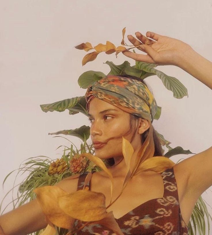 This may contain: a painting of a woman with leaves on her head and hands above her head, holding plants in front of her face
