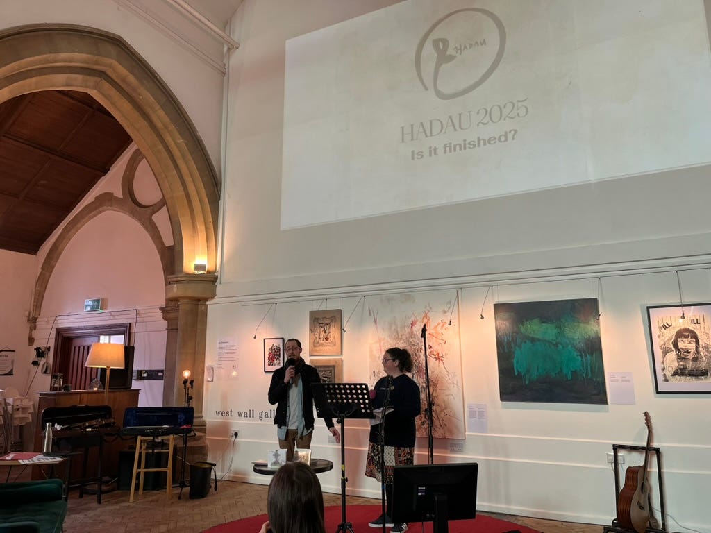 Hadau 2025 - two presenters speaking in a beautiful church building in front of an exhibition wall of art Hadau 2025 - two presenters speaking in a beautiful church building in front of an exhibition wall of art