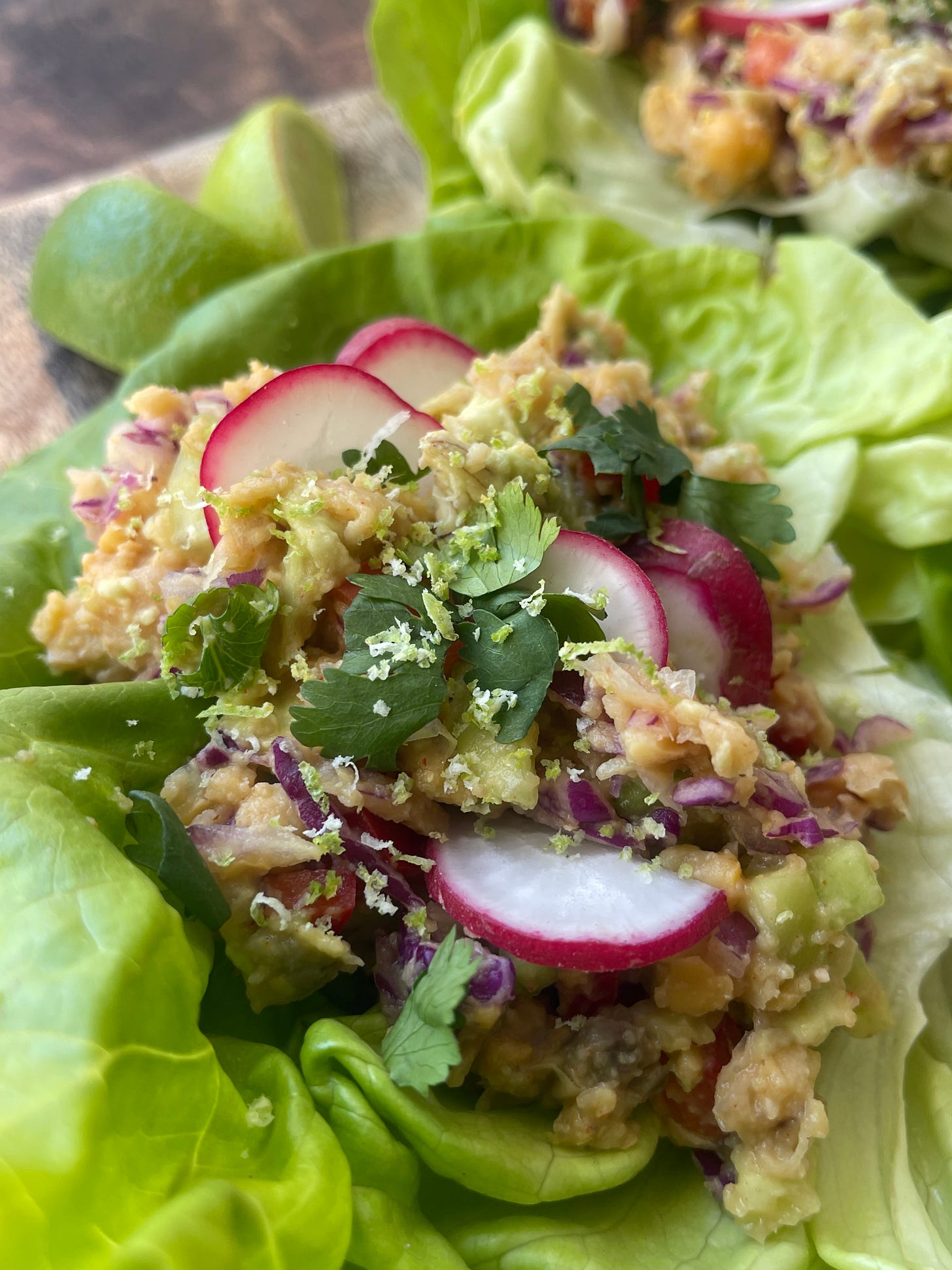 Close-up of a Pharmaka lettuce wrap filled with smashed chickpea and tahini mixture, topped with sliced radishes, fresh cilantro, and lime zest in a butter lettuce cup
