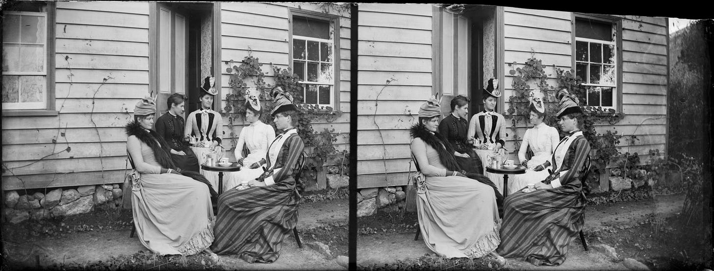 a black and white photo of 5 women sitting outside of a house drinking tea