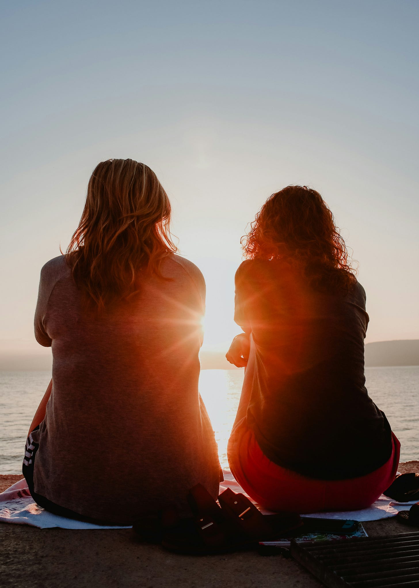 Two women sitting by the water, watching the sunset.