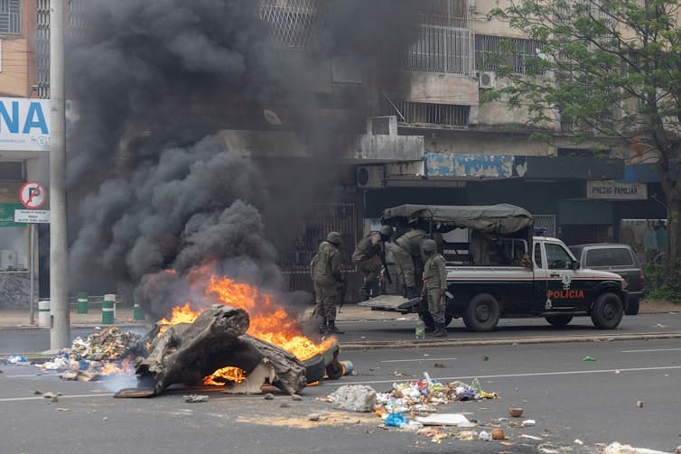 Anti-riot police officer next to a burning barricade in Maputo in November 2024. Anti-riot police officer next to a burning barricade in Maputo in November 2024.