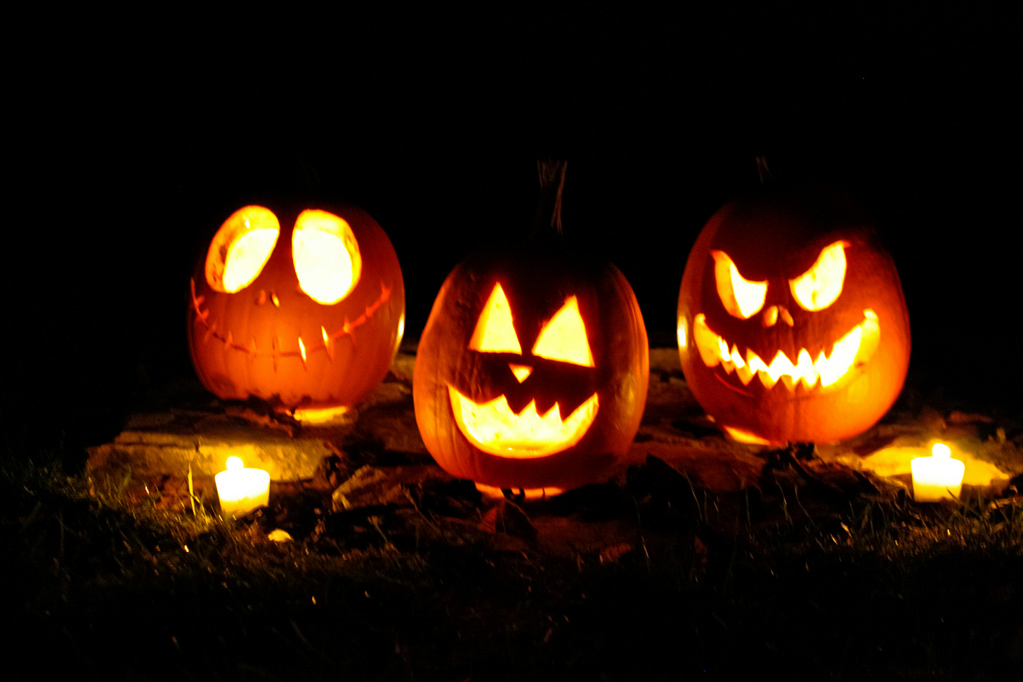 three carved pumpkins with candles inside them