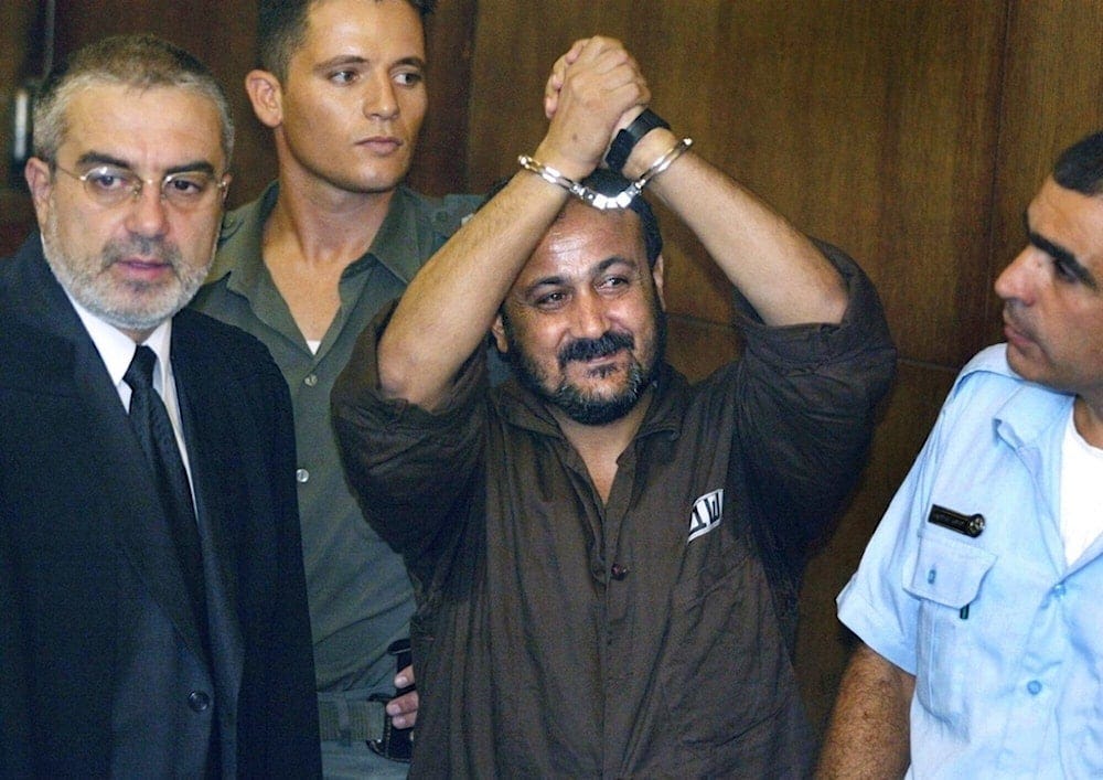 Marwan Barghouti, center, raises his handcuffed hands in the air on the opening day of his trial in Tel Aviv, occupied Palestine, Aug. 14, 2002. (AP Photo/Brennan Linsley, File) Marwan Barghouti, center, raises his handcuffed hands in the air on the opening day of his trial in Tel Aviv, occupied Palestine, Aug. 14, 2002. (AP Photo/Brennan Linsley, File)