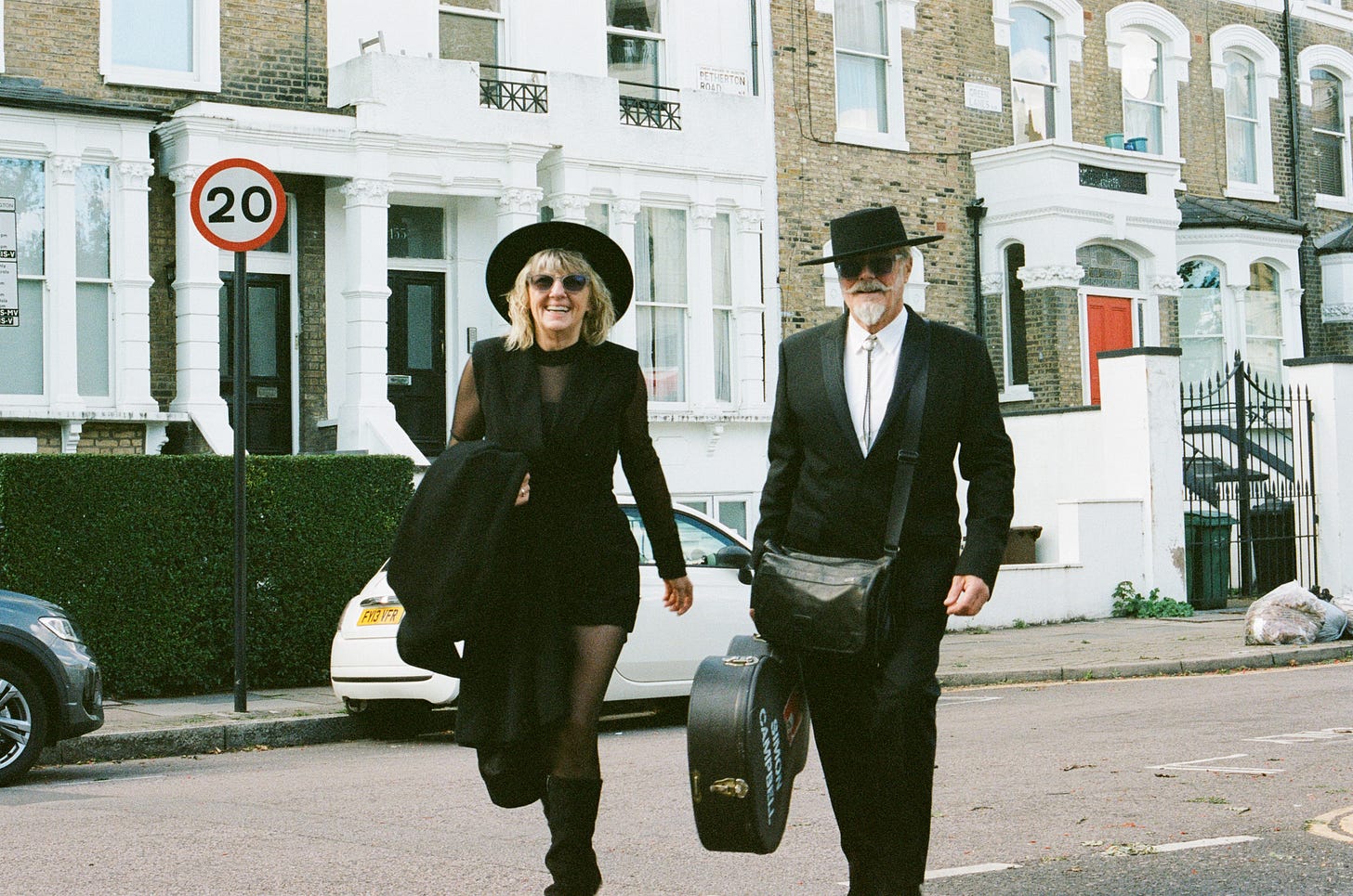 A woman wearing a hat and a man wearing a hat carrying a guitar