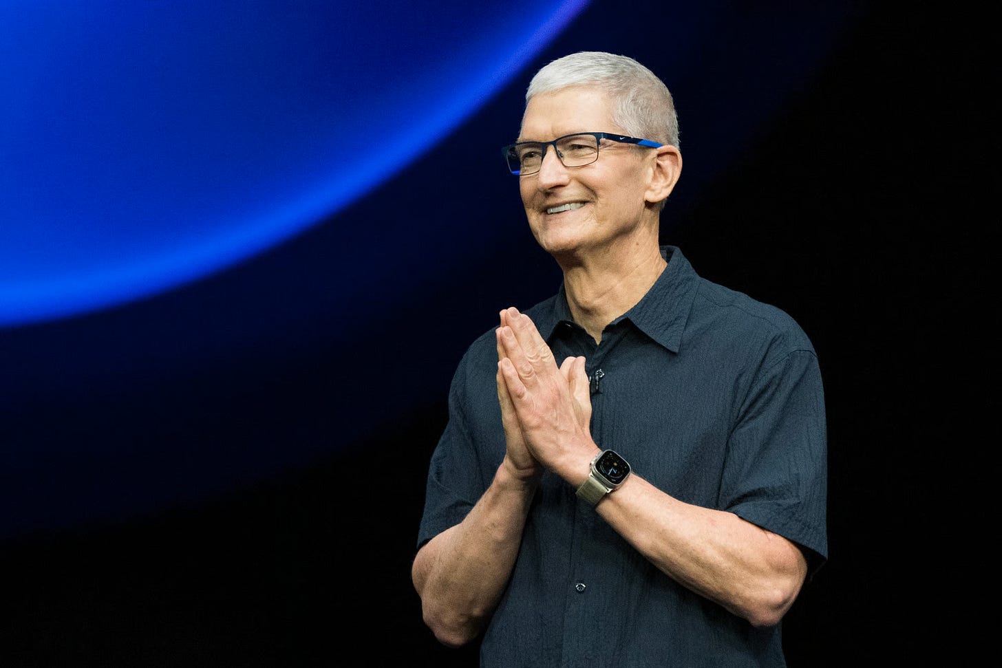 Tim Cook smiling with hands clasped, Apple CEO known for strict stance on leaks. Tim Cook smiling with hands clasped, Apple CEO known for strict stance on leaks.