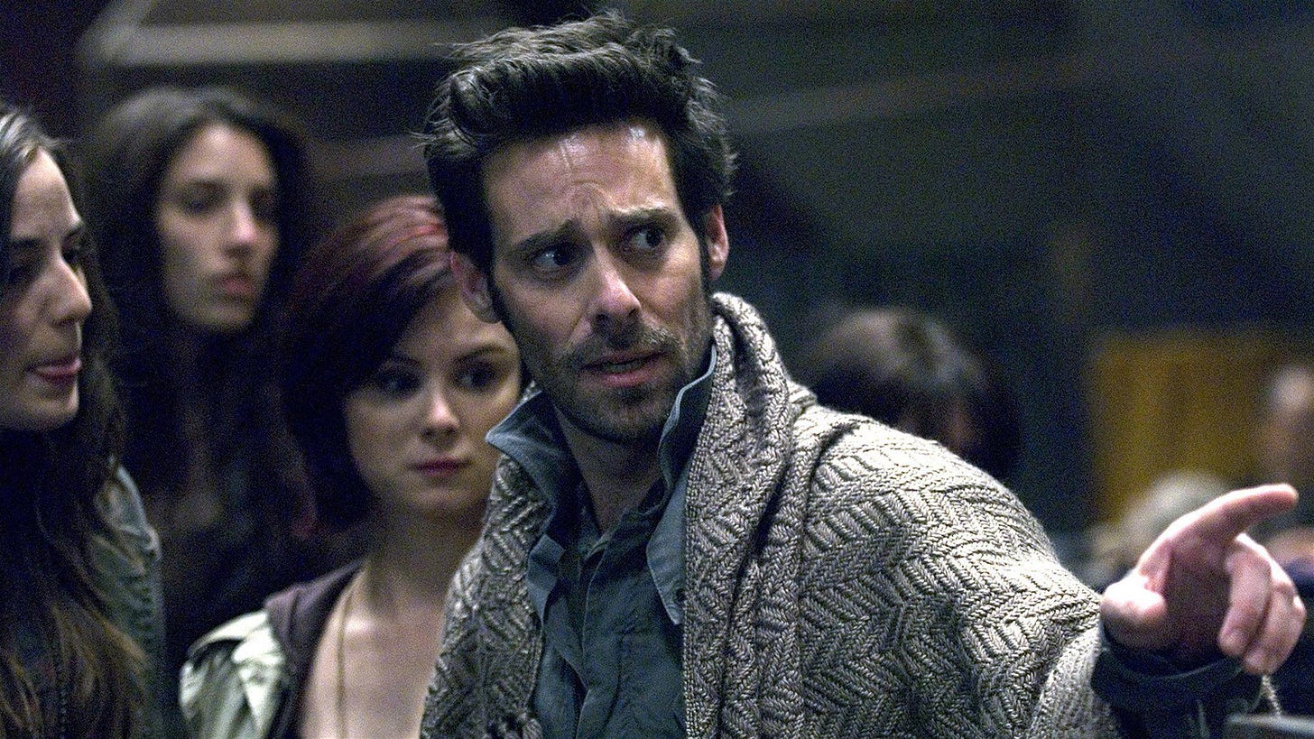 Gaius Baltar (James Callis) has a blanket over his shoulders. Gaius Baltar (James Callis) has a blanket over his shoulders.
