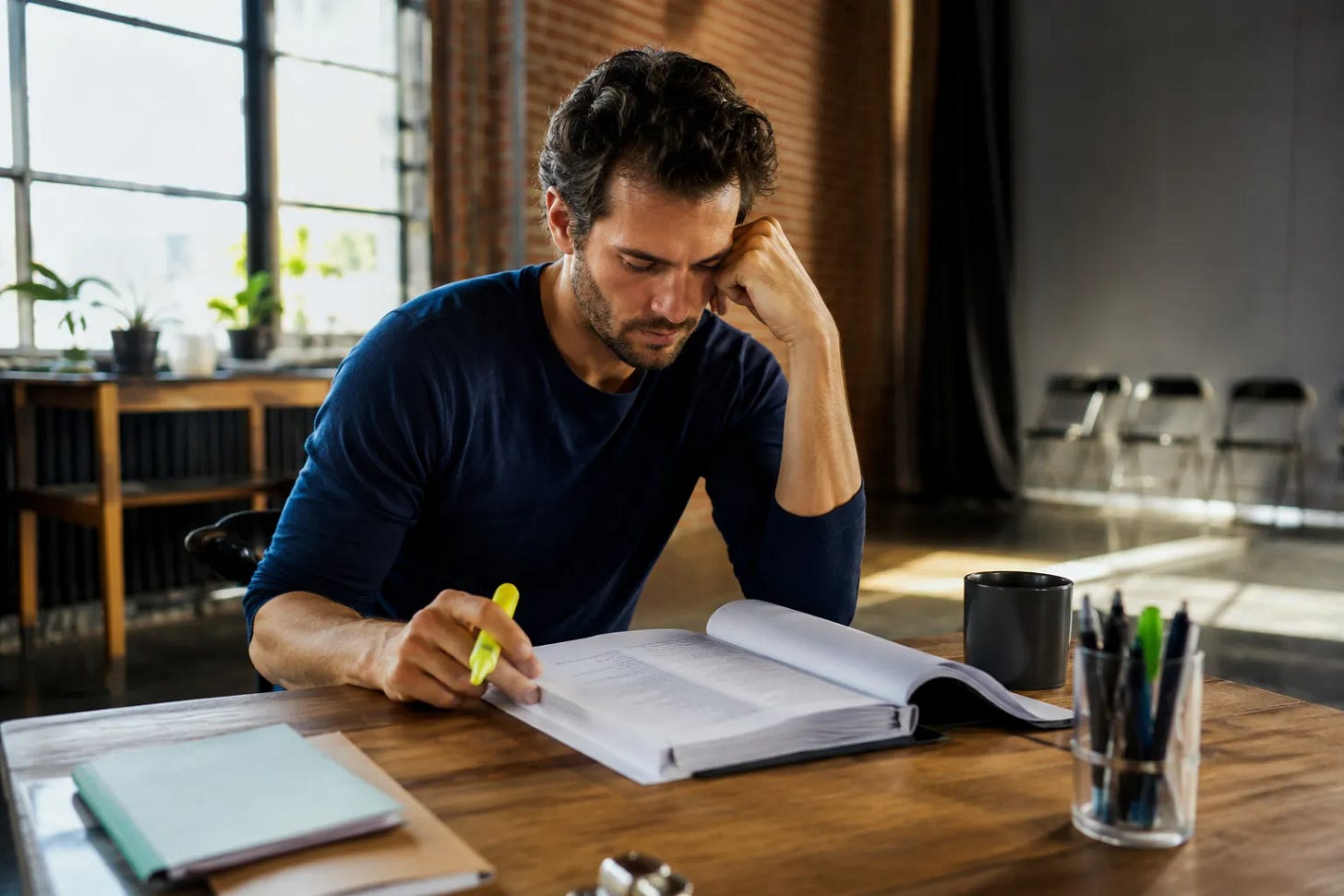 An actor at a sunlit table marking up script sides with a highlighter