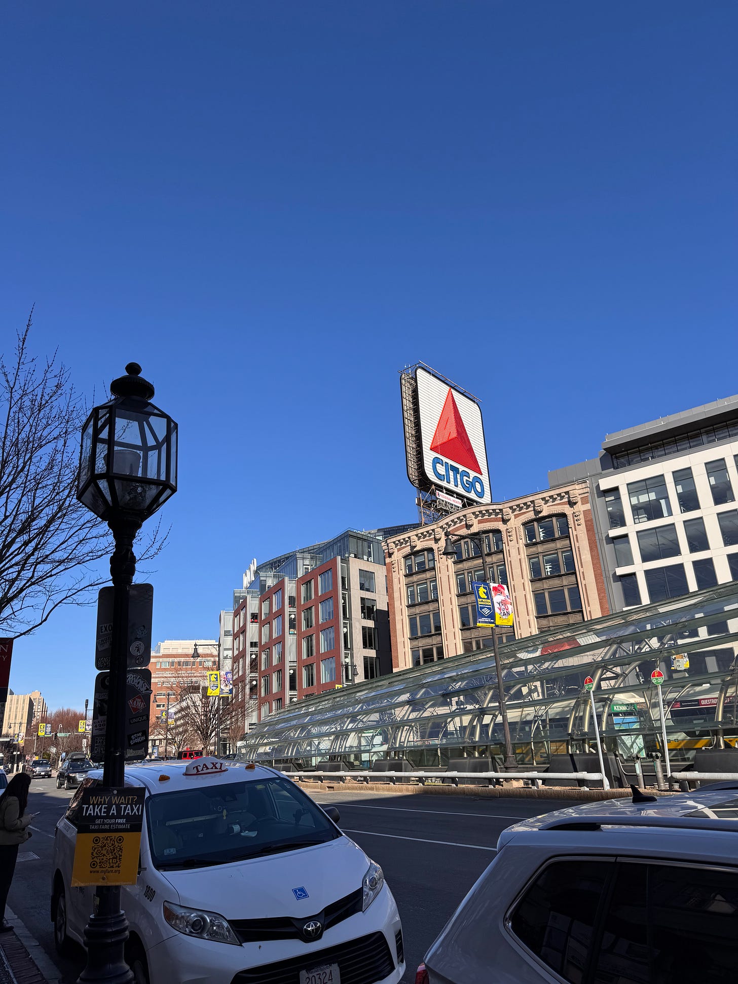 Morning shot from the Fenway/Kenmore neighborhood of Boston. Street traffic in the foreground, the famous Boston CITGO sign in the background against a bright blue sky.