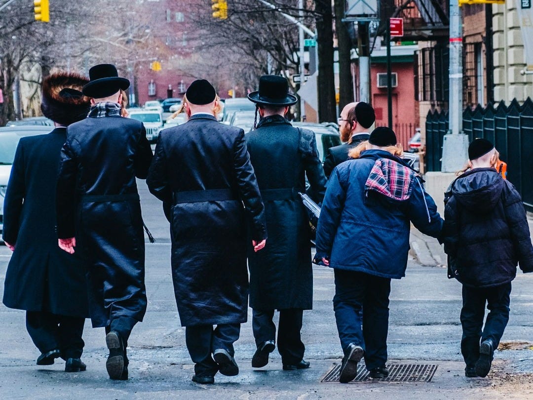 group of men in black coat walking on sidewalk during daytime group of men in black coat walking on sidewalk during daytime
