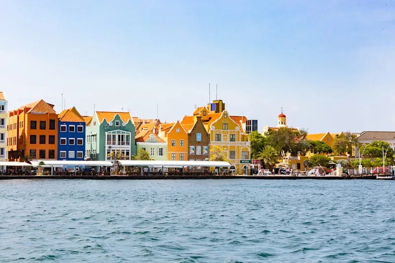 Waterfront view of colorful colonial-era buildings in Willemstad, Curaçao, painted in bright yellow, blue, green, and orange along the water.