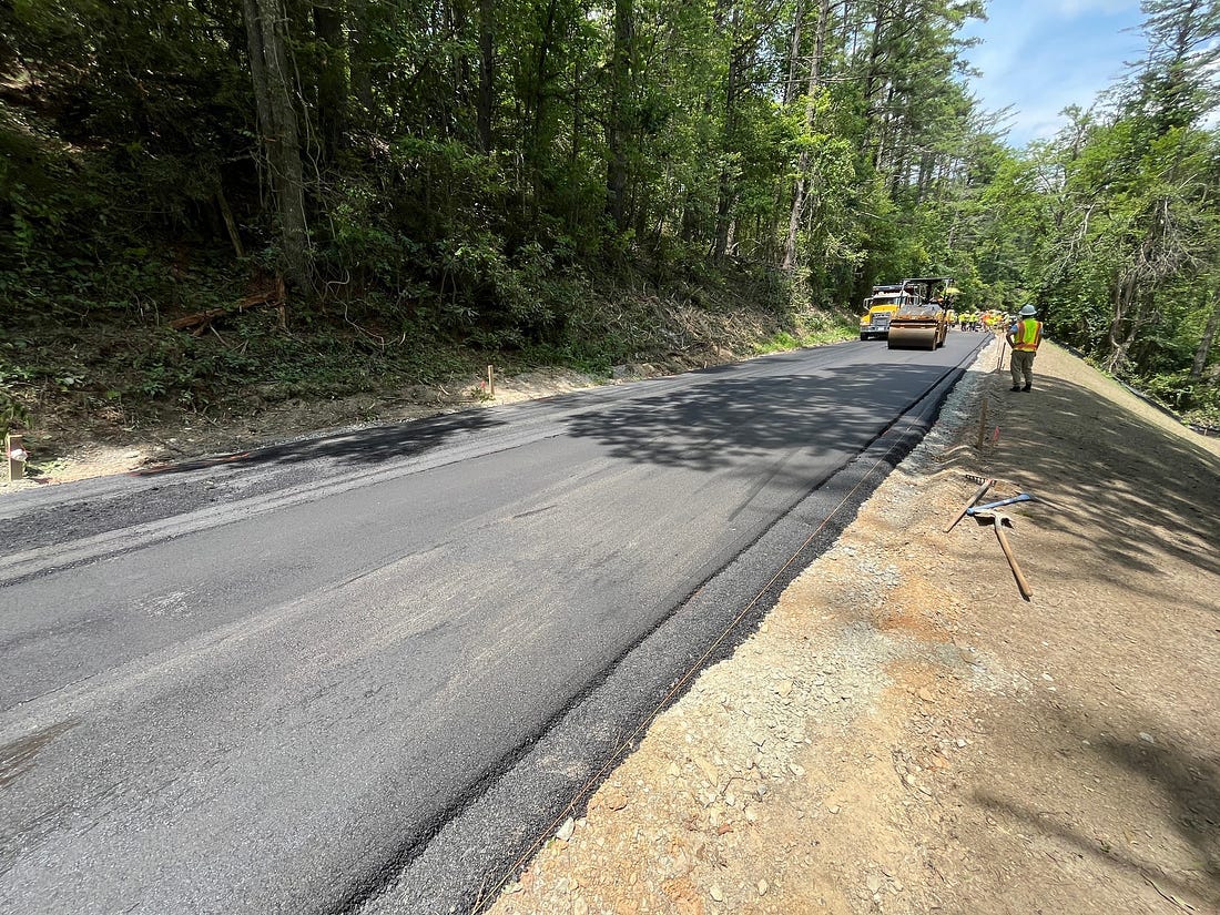 Construction equipment and workers paving the road at milepost 224.9 with the slope that was recently rebuilt in the foreground with a layer of fill dirt on top. 