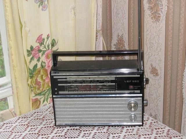 This may contain: an old fashioned radio sitting on top of a table next to a window with floral curtains