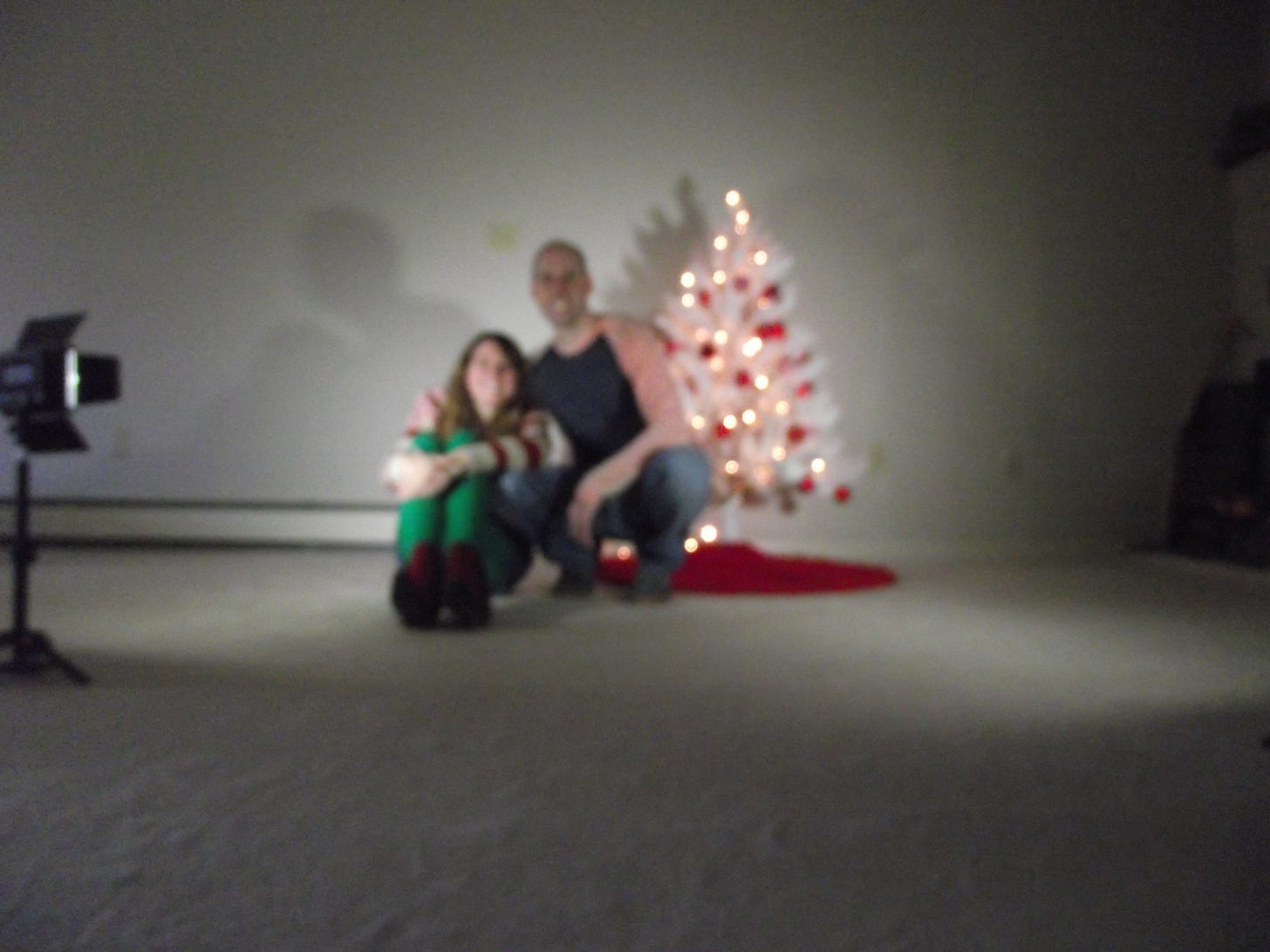 A blurry out of focus Christmas card photo of a couple beside a white Christmas tree.