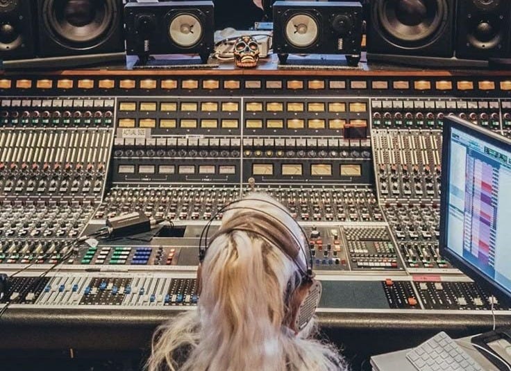 This may contain: a woman sitting in front of a mixing desk with sound equipment on top of it