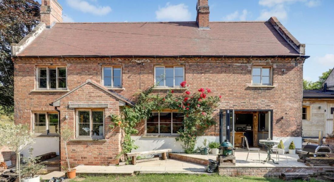 A brown brick cottage with windows, a lawn in front of it, and a blue sky behind it A brown brick cottage with windows, a lawn in front of it, and a blue sky behind it