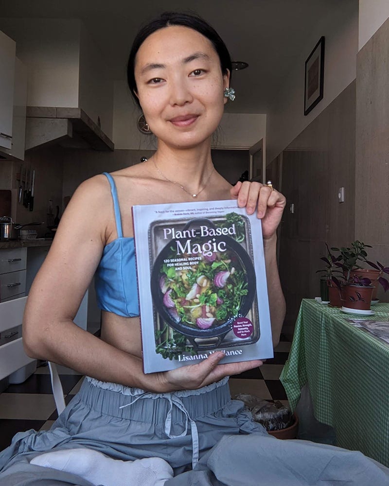 Photo of a person smiling and holding up the cookbook "Plant-Based Magic" by Lisanna Wallance. Photo of a person smiling and holding up the cookbook "Plant-Based Magic" by Lisanna Wallance.